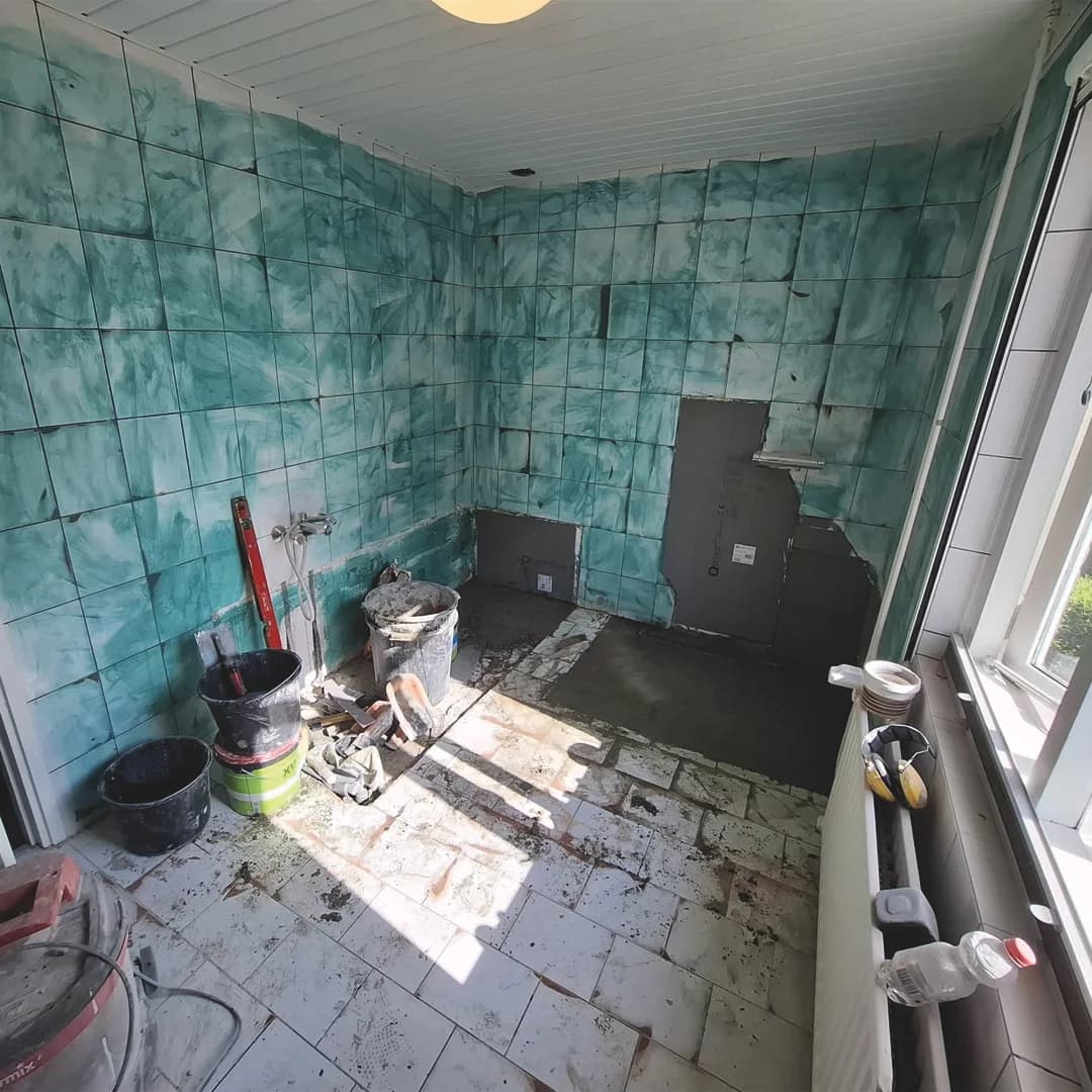 Badkamer in verbouwing uit eigen werk: het oude groene wandtegelwerk is deels weggehaald, de vloertegels liggen er gedeeltelijk uit en de ondervloer ligt open.